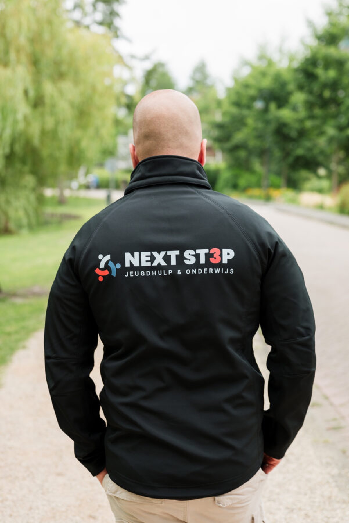 NEXT ST3P-coach loopt buiten in een jas met het logo op de rug